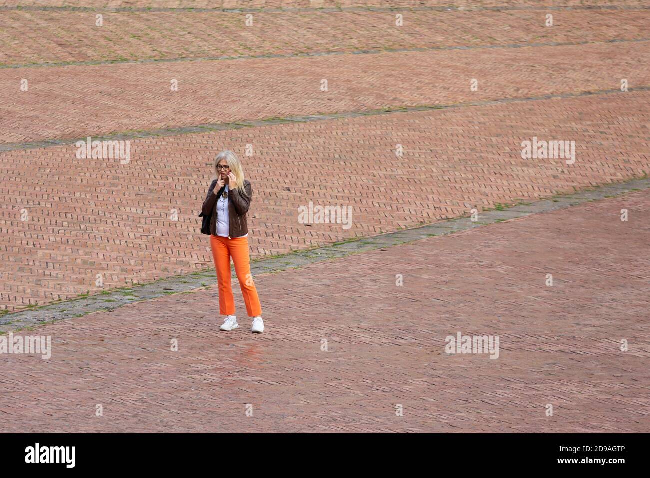 Eine Frau in leuchtend orangefarbenen Hosen spricht am Telefon auf der Piazza del Campo, Siena, Toskana, Italien Stockfoto