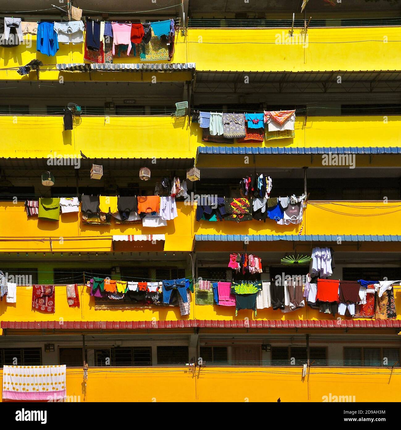 Bunte Wäsche zum Trocknen auf den gelben Balkonen eines Wohnblocks mit hoher Dichte in Asien. Stockfoto