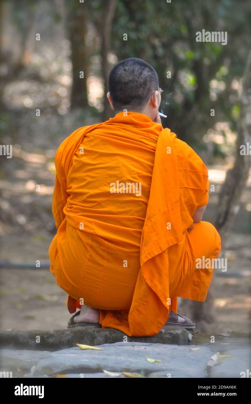 Rückansicht eines buddhistischen Mönchs in Safranroben, der eine Zigarette raucht. Stockfoto