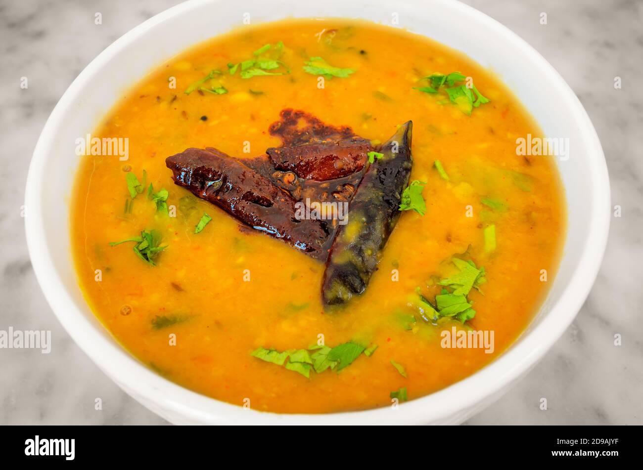 Indische Schale Linsen (Dal) Curry in einer weißen Schüssel garniert Mit trockenen Chilis und Korianderblättern Stockfoto