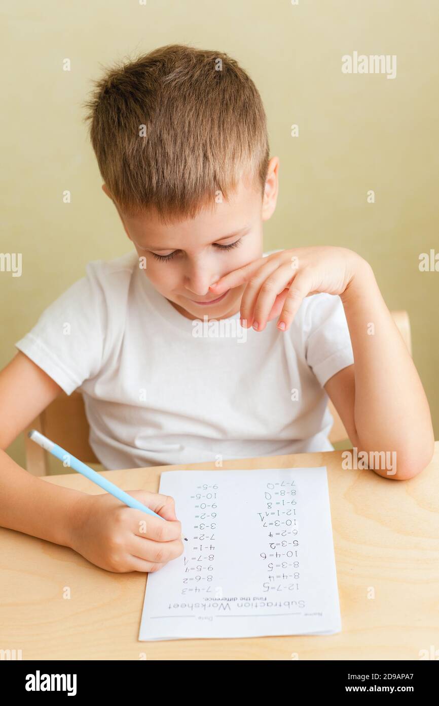 Nahaufnahme Porträt von niedlichen Jungen zu Hause lernen. 7 Jahre altes Kind, das Mathematik-Unterricht macht, sitzt am Schreibtisch in seinem Zimmer. Stockfoto