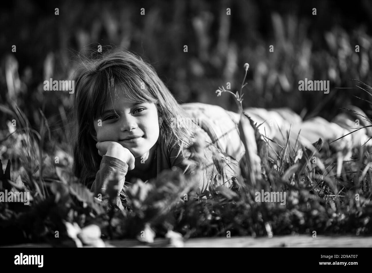 Kleines Mädchen liegt im Gras im Park. Schwarzweiß-Foto. Stockfoto