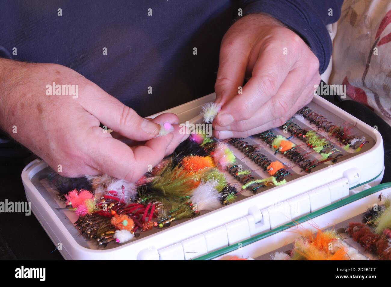 Nahaufnahme reifen mans Hände Putting seine Hand gemacht Angeln Fliegt in seine weiße Angelkasten Stockfoto