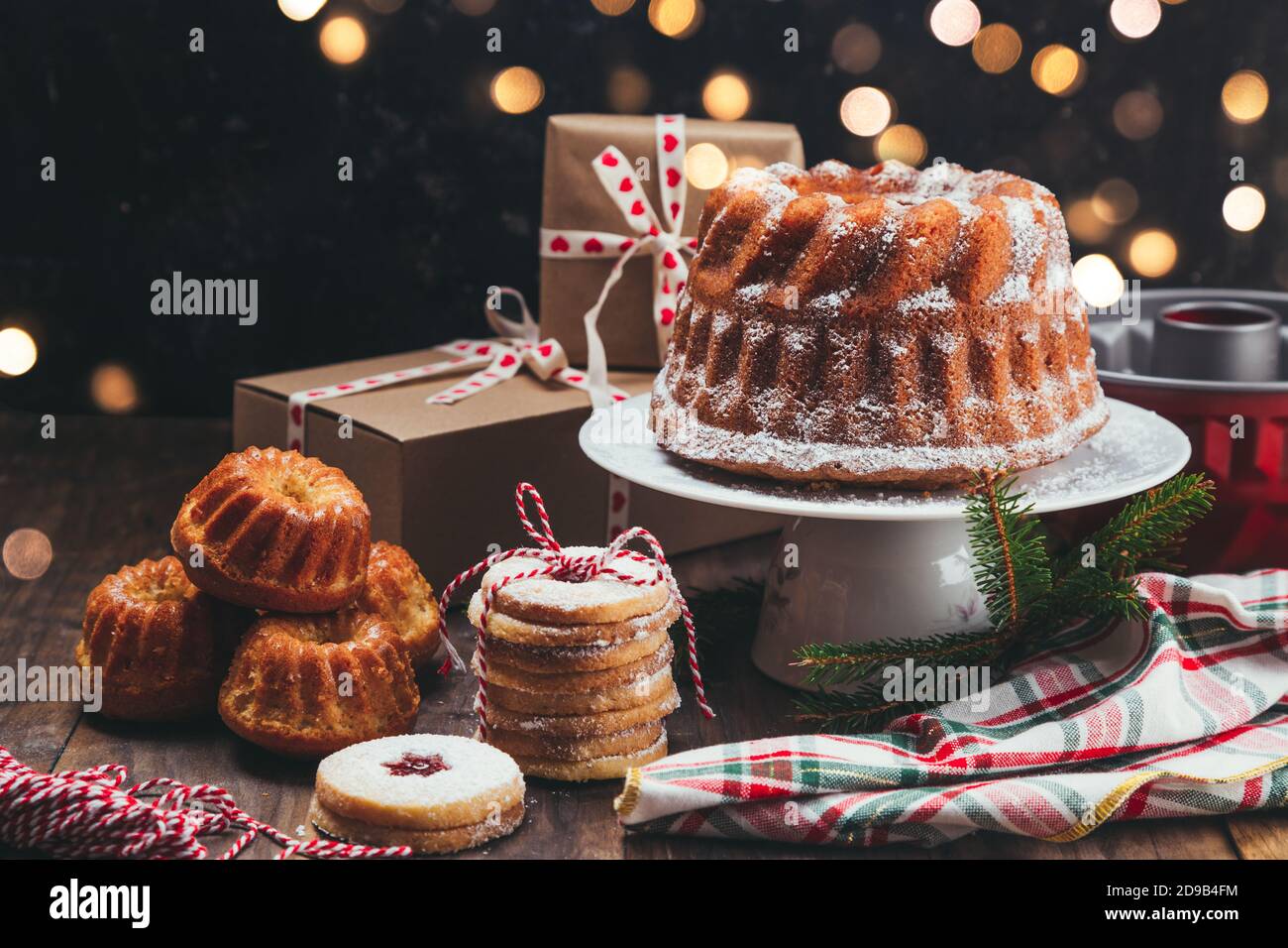Auswahl an hausgemachten Weihnachtsdesserts und Geschenkschachteln auf einem Rustikaler Holztisch mit Weihnachtsbeleuchtung Stockfoto