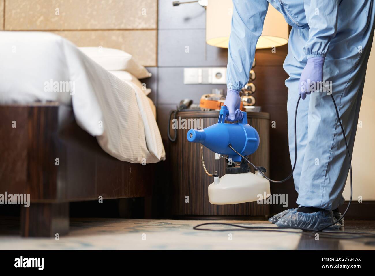 Arbeiter in Schuhüberzügen, die Desinfektionsmittel benutzen, während sie im Hotelzimmer stehen. Coronavirus und Quarantänekonzept Stockfoto
