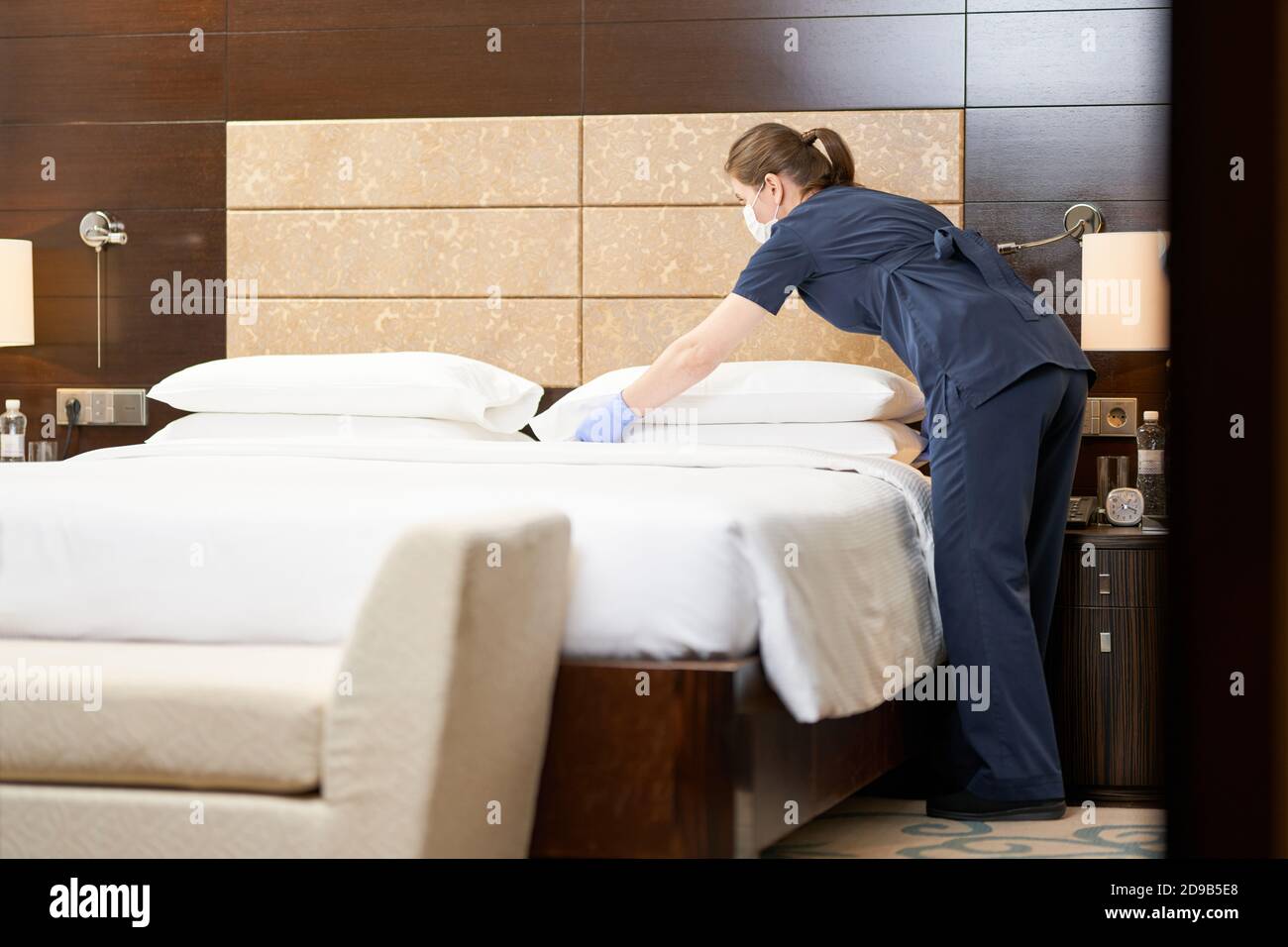 Foto in voller Länge von Zimmermädchen, die das Bett gemacht und die Bettwäsche im Schlafzimmer gewechselt hat. Servicekonzept des Hotels Stockfoto