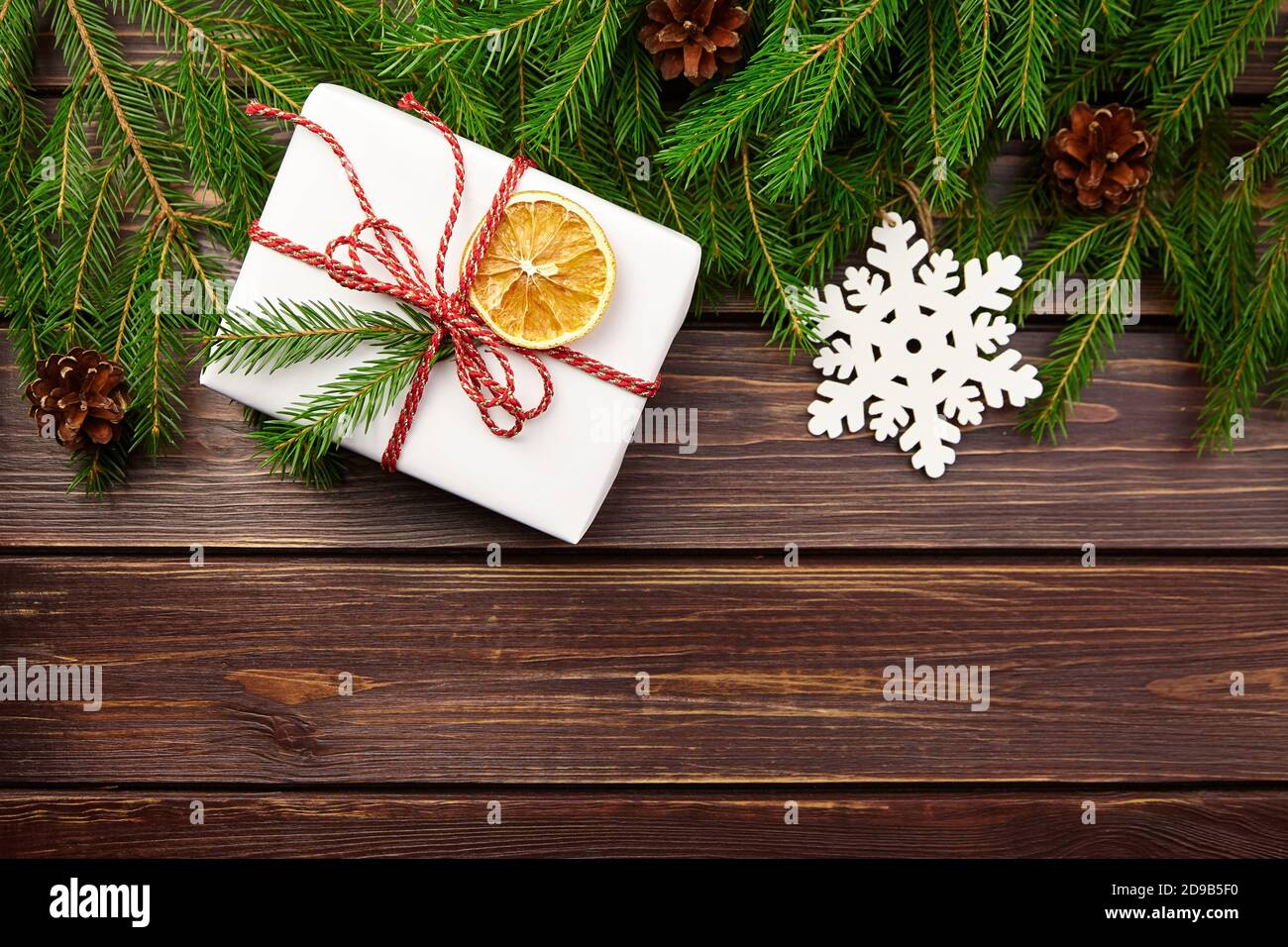 Weihnachts-Geschenkbox mit Tannenzweigen, Zapfen und Schneeflocken auf Holzhintergrund Stockfoto