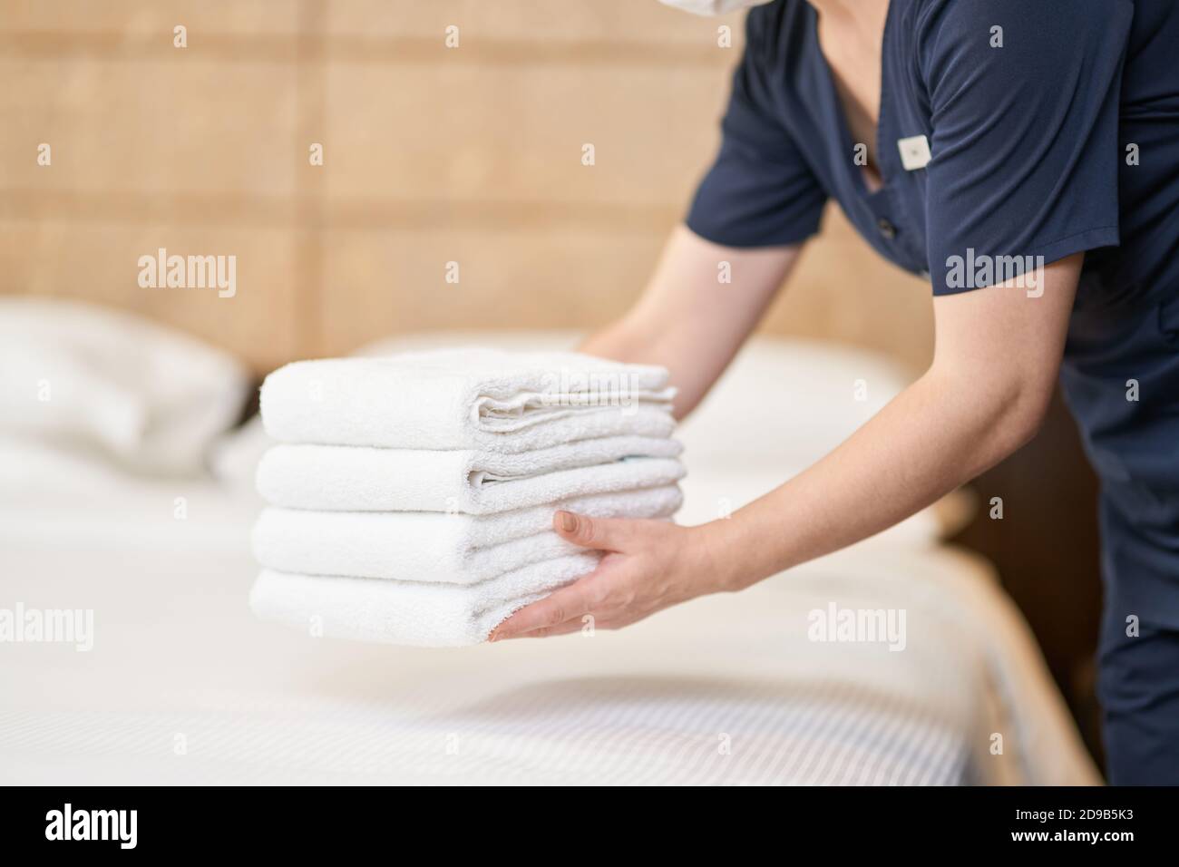 Zugeschnittenes Foto von Zimmermädchen in Uniform, die Stapel sauberer Handtücher im Zimmer im Hotel hielt. Servicekonzept des Hotels Stockfoto