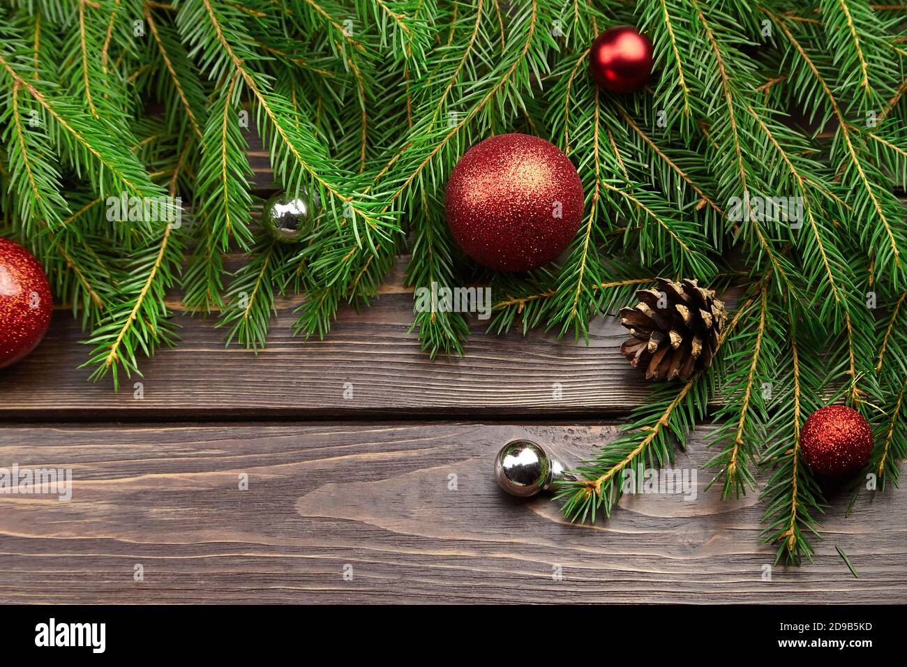 Winterurlaub Dekorationen mit Tannenzweigen auf dunklem Holzhintergrund. Weihnachtskomposition mit roten Kugeln und Zapfen Stockfoto