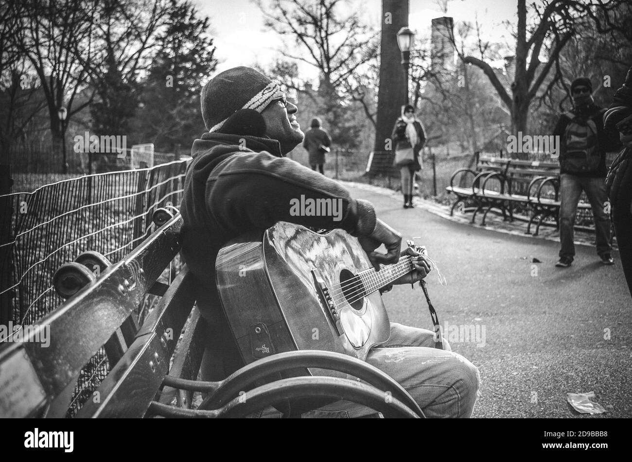 Ein fröhlicher Straßenmusiker spielt klassische Gitarre auf einer Bank. Schwarzweiß-Fotografie Stockfoto