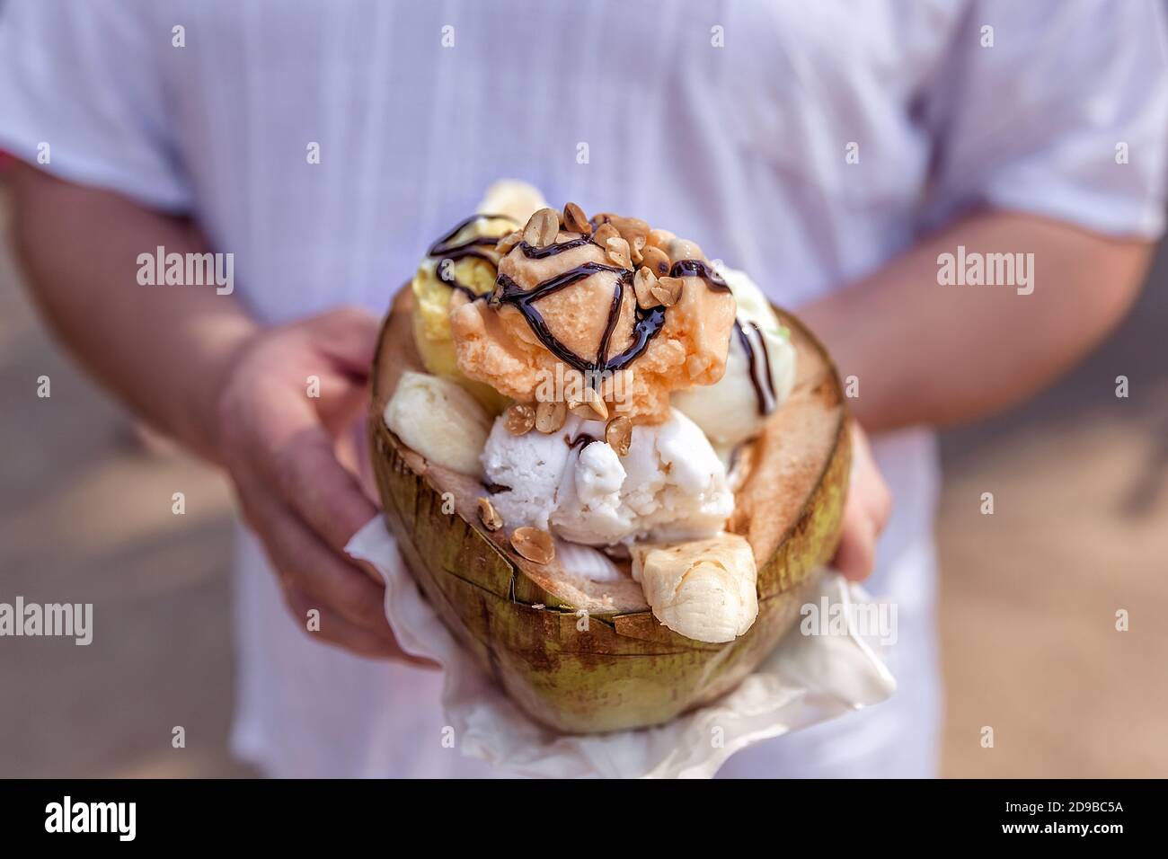 Nüsse und Banane mit Schokolade Belag auf Eis. Eis in einer Kokosnuss in den Händen halten. Nahaufnahme. Stockfoto