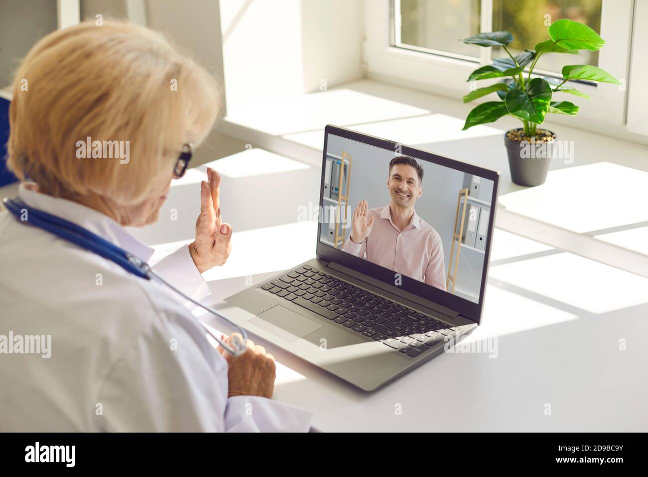 Die ältere Ärztin und ihre Patientin winken einander in einem Video-Chat an. Stockfoto