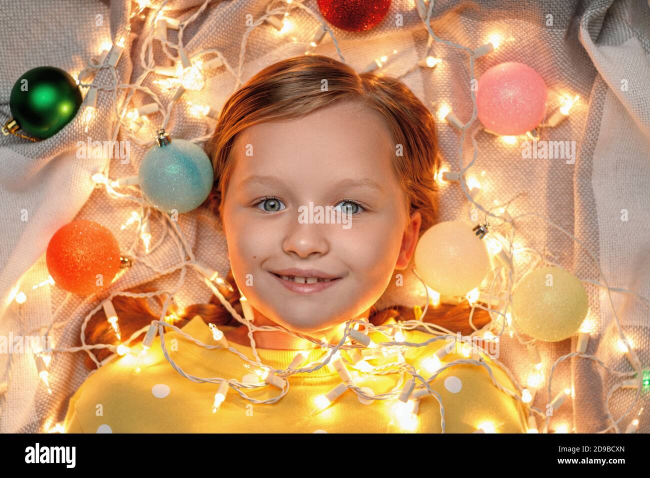 Draufsicht auf ein kleines Mädchen, das in einer glühenden Weihnachtsgirlande liegt. Stockfoto