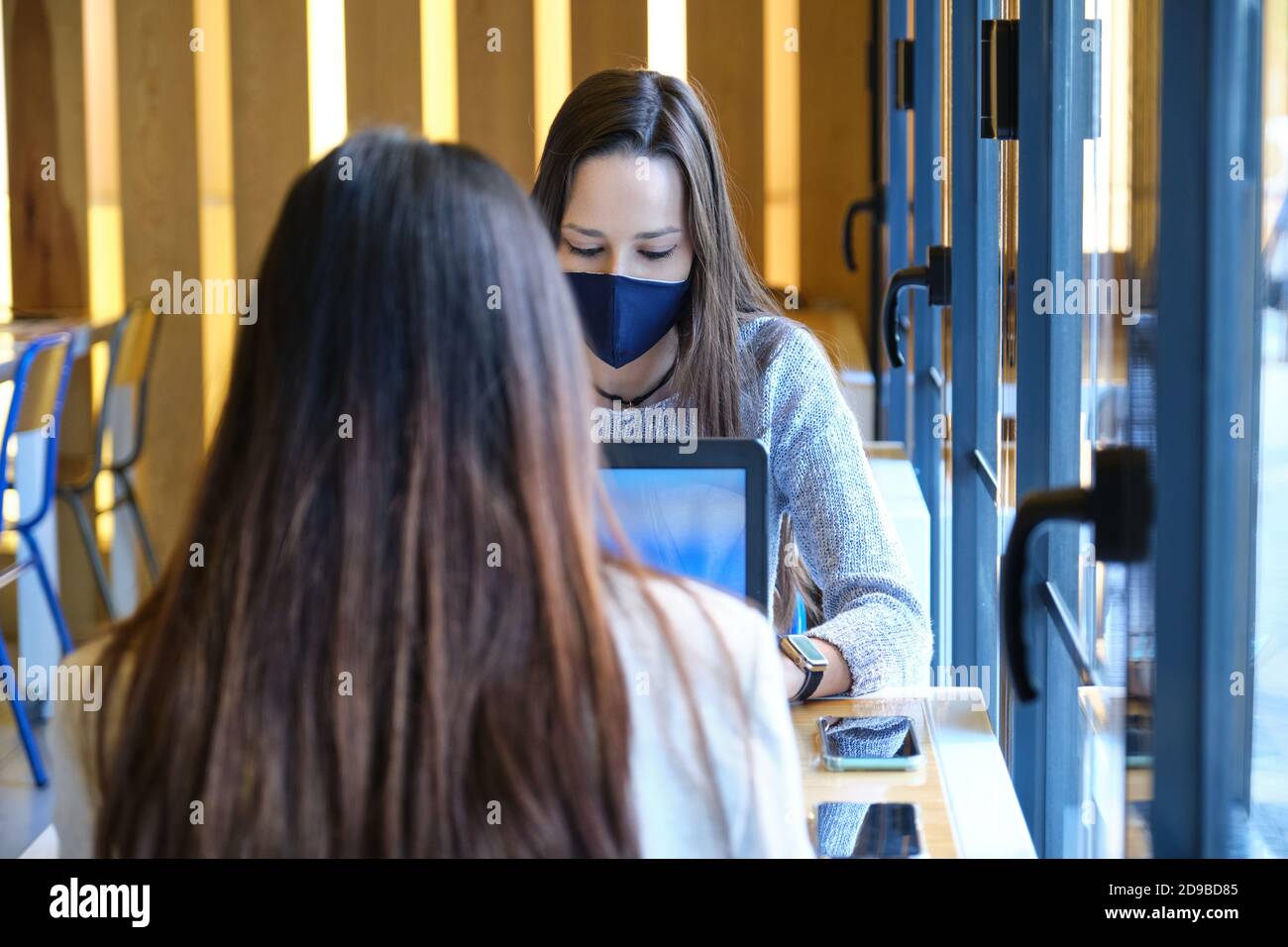 Zwei Schülerinnen mit Gesichtsmasken, die in einem Restaurant an ihren Computern arbeiten. Neue Normalität in Restaurants. Coronavirus-Pandemie. Stockfoto