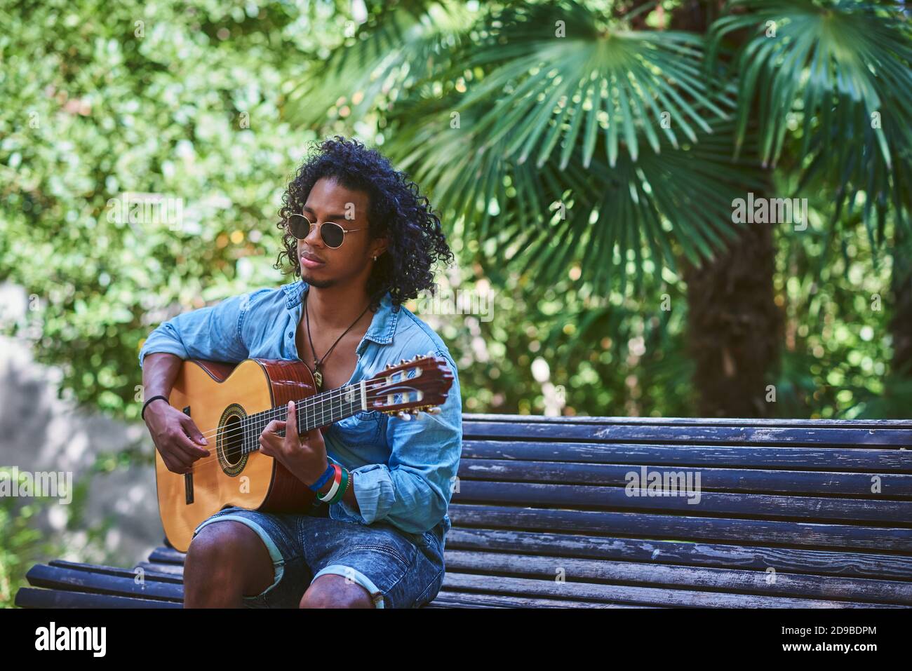 Musiker spielt Gitarre in einem schönen Park. Er ist von Vegetation umgeben. Stockfoto