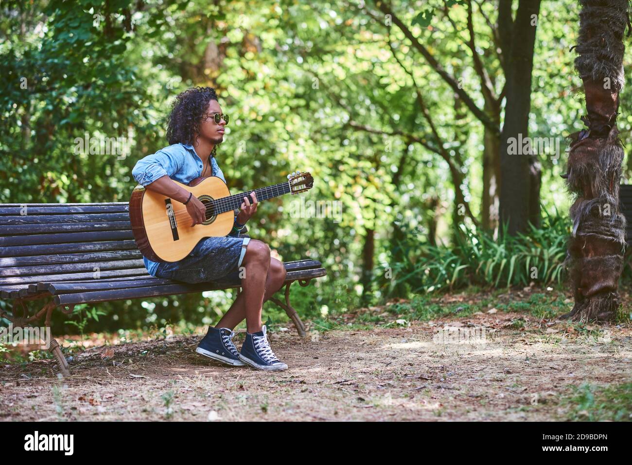 Musiker spielt Gitarre in einem schönen Park. Er ist von Vegetation umgeben. Stockfoto