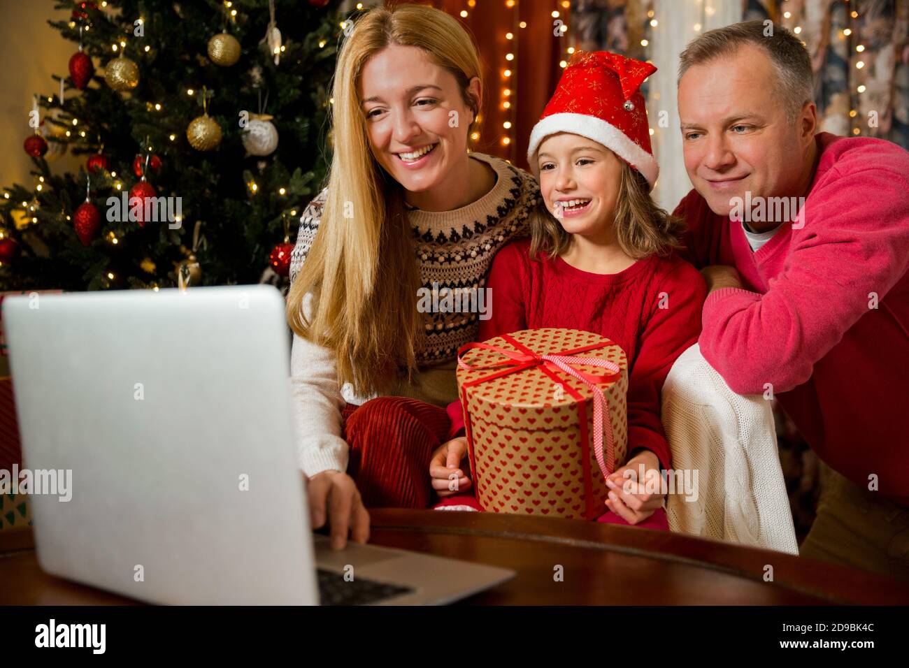 Ein glückliches Paar mit einem Kind feiert Weihnachten mit ihren Freunden auf Videoanruf mit Webcam. Familie begrüßt ihre Verwandten am Heiligabend Stockfoto