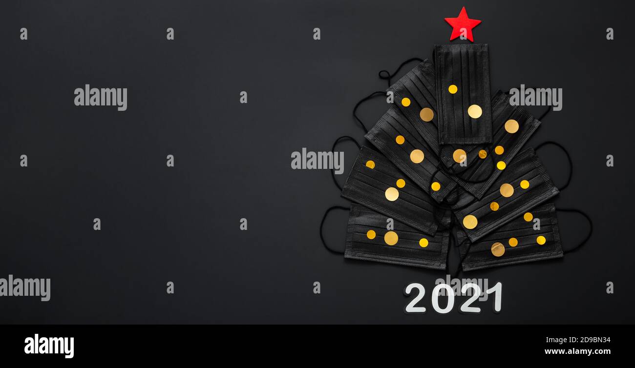 Weihnachtsbaum aus Gesichtsmasken und Gold festliche Dekor Konfetti. Gesichtsmasken auf schwarzem Hintergrund. 2021 Einladungskarte für Silvester mit Kopie Stockfoto