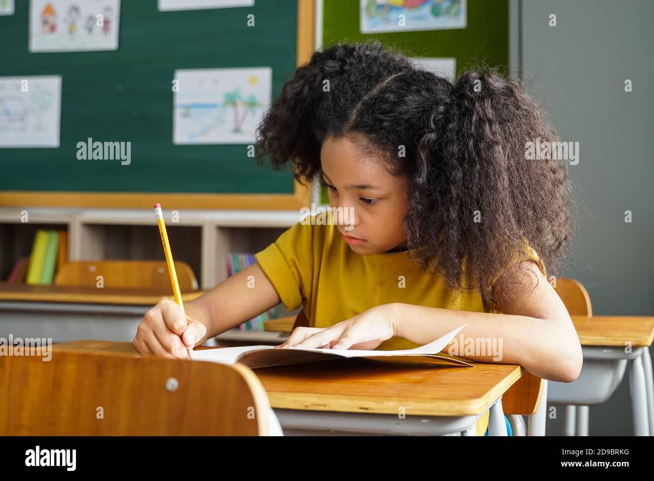 Afroamerikanische Schulmädchen sitzen in der Schule schriftlich in Notiz Buch mit Bleistift, Studium, Bildung, Lernen. Studentin am Schreibtisch im Klassenzimmer in der Prüfung. Stockfoto