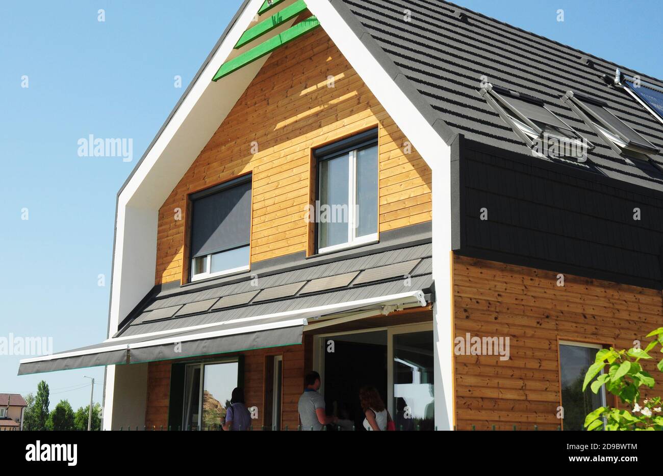 Modernes energieeffizientes Holzhaus mit Oberlichtern und Solarpaneel auf Asphalt Schindle Dach, Fenster mit Rollläden und Outdoor-Baldachin Dach. Stockfoto