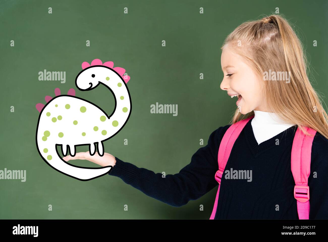 Schulmädchen zeigt mit der Hand auf illustrierte Dinosaurier auf grünen Kreidetafel Stockfoto