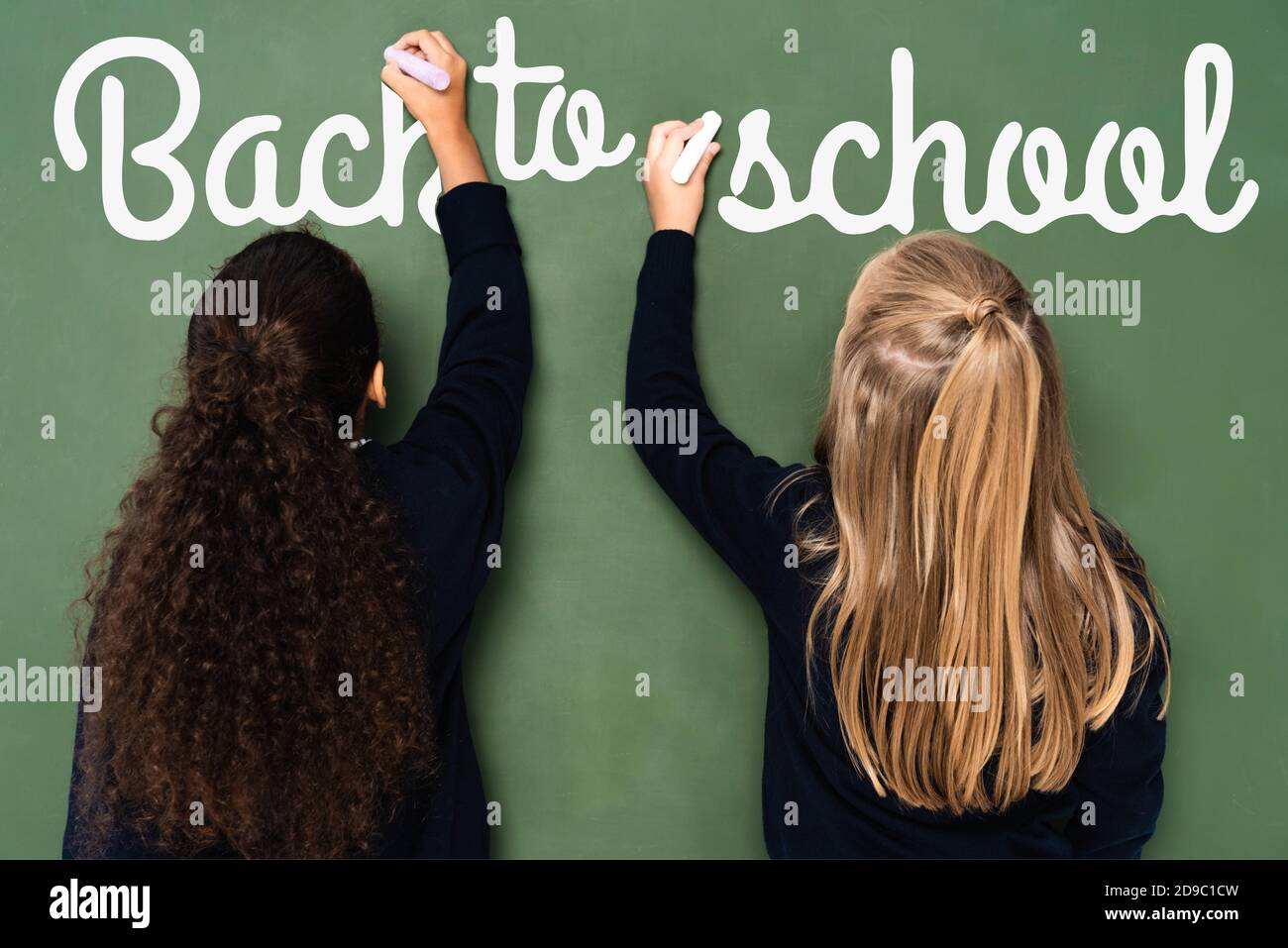 Rückansicht von multikulturellen Schülerinnen schreiben zurück zur Schule Schriftzug Auf dem Schwarzen Brett Stockfoto