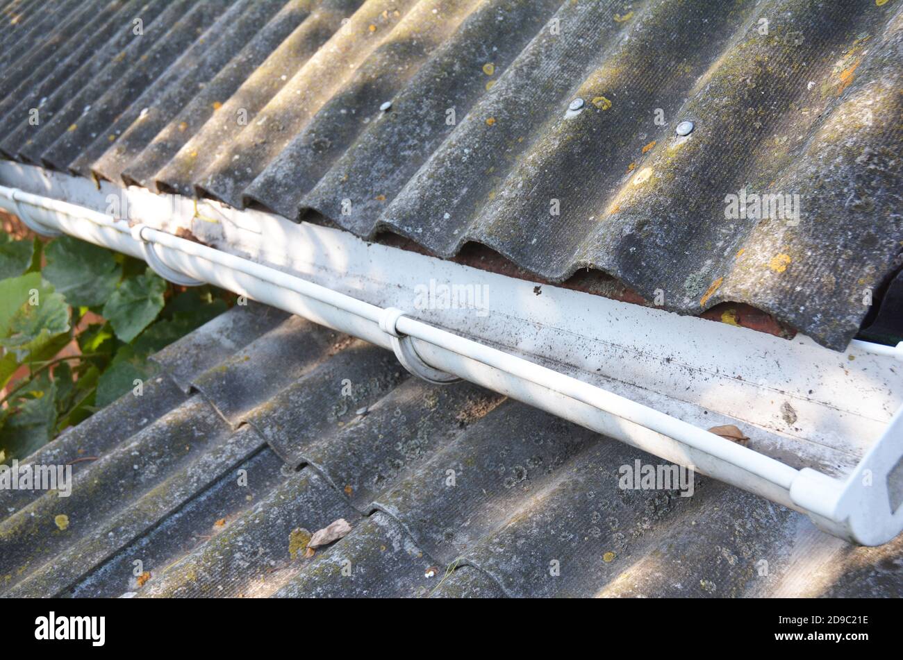 Eine Nahaufnahme einer alten Asbest-Doppeldachkonstruktion mit einer Kunststoff-Regenrinne, die von heruntergefallenen Blättern und Schmutz gereinigt wurde. Stockfoto