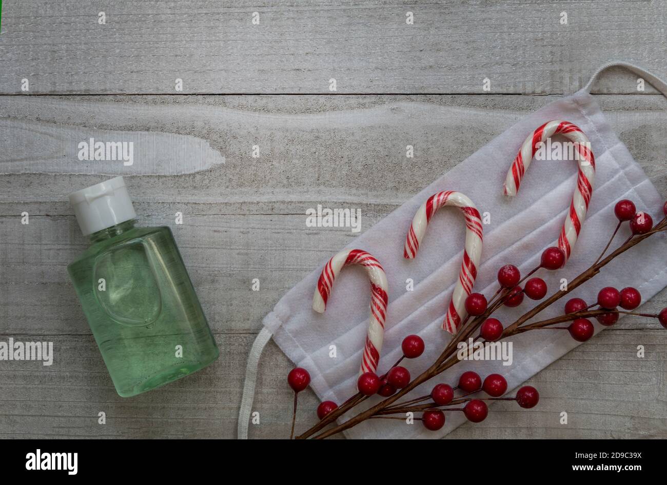 Maske und Handdesinfektionsmittel sicher gesunde Feiertage Konzept mit festlichen Candy Stöcke und rote Beeren grau Hintergrund flach Lay Kopie Platz Stockfoto