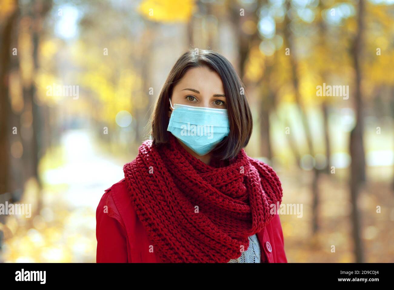 Schöne Frau in medizinischen Schutz Gesichtsmaske zu Fuß im Freien im Herbst Park. Coronavirus soziale Distanz Konzept. Stockfoto