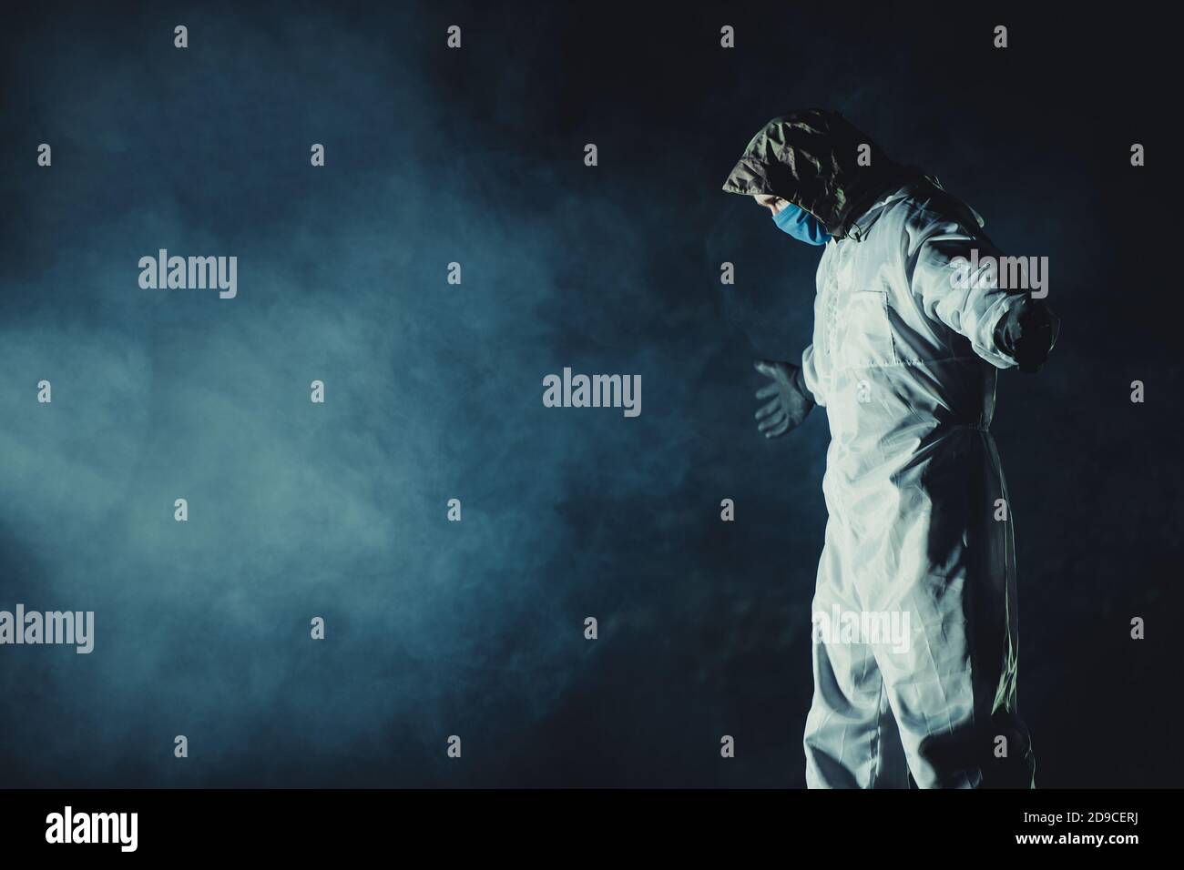 Kaukasische Männer tragen blaue Maske und Gefahrgut Anzug in dunklen rauchigen Ort mit gestreckten Händen. Konzeptionelles Foto. Stockfoto