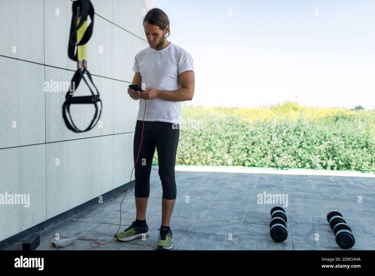 Outdoor-Training.Slim Mann mit langen Haaren. Blick auf das Smartphone während einer Pause von seiner Routine. Stockfoto