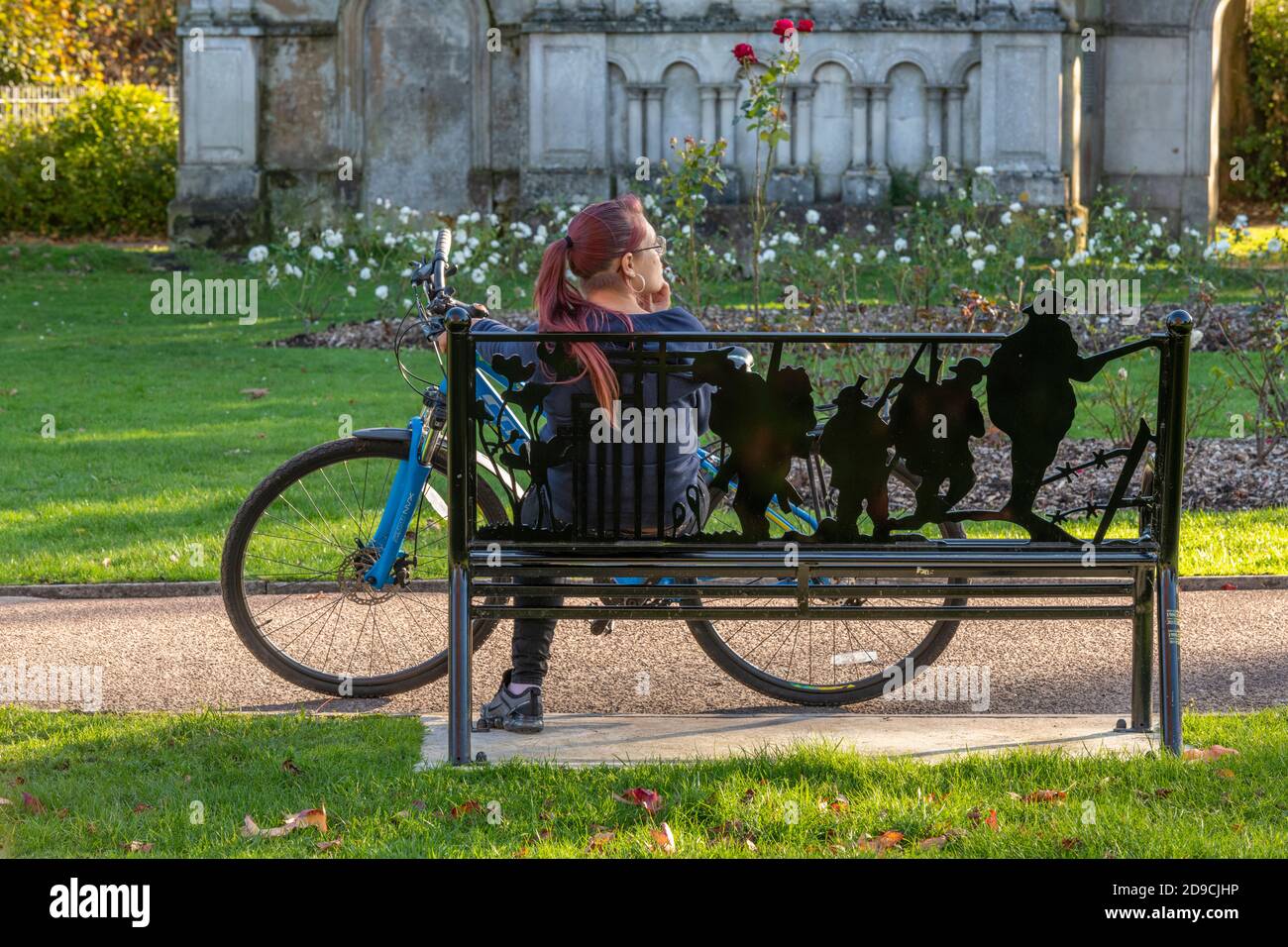 Junge Frau, die auf einer Bank unter einem Herbstbaum sitzt Rast während einer Radtour an einem sonnigen Herbsttag Stockfoto