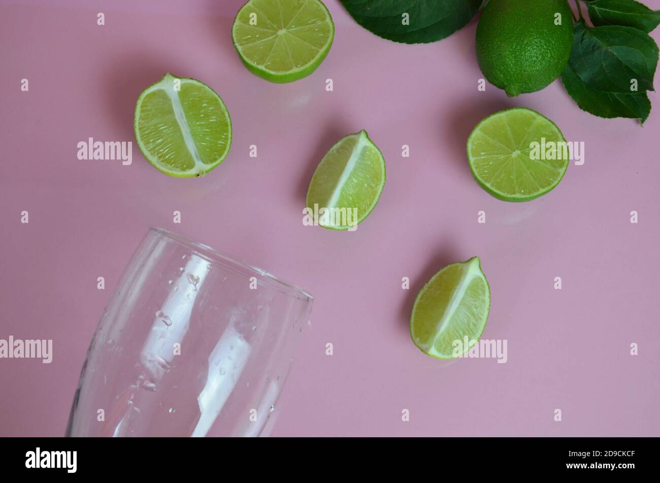 Zutaten für Mojito auf rosa Hintergrund. Leeres Glas, Stroh, Minze, Limette, Eiswürfel. Limette und Minze fallen in einen Cocktail spritzt Stockfoto