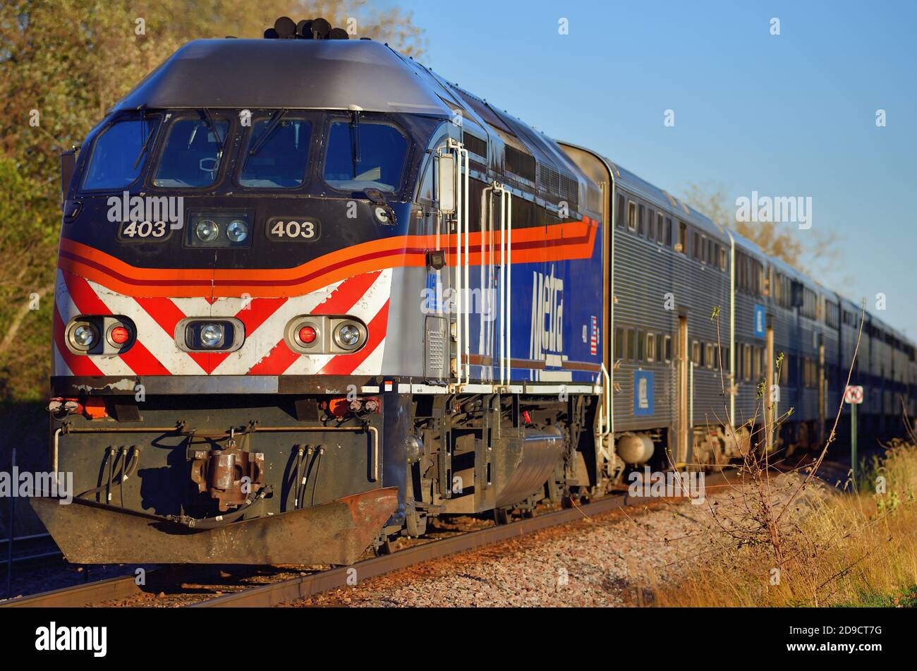 Bartlett, Illinois, USA. Ein Metra Pendlerzug, der zu seinem späteren Ziel Chicago geschoben wird, wird durch die späte Nachmittagssonne hervorgehoben. Stockfoto