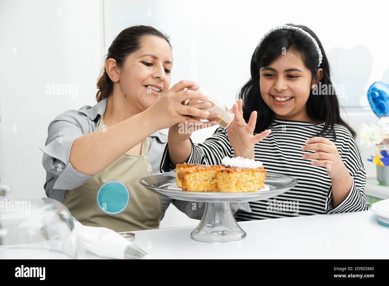 Hispanische Mutter und Tochter dekorieren einen Kuchen mit Schlagsahne - Latein Mutter lehrt ihre Tochter, einen Kuchen zu dekorieren - Mutter und Tochter haben Spaß c Stockfoto