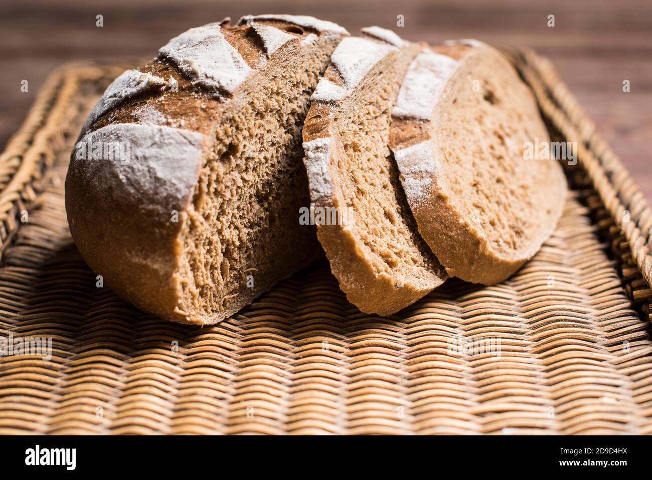 Laib braunes Brot mit zwei Scheiben auf einem geschnitten Braunes Weidenblech Stockfoto