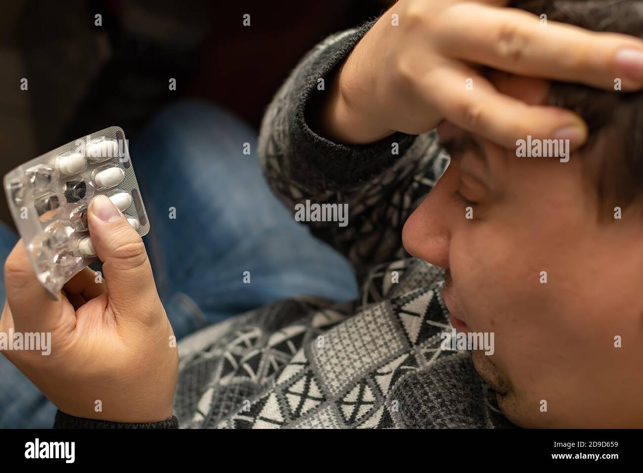 Eine Packung Pellets, Pillen in der Hand einer Person mit schlechter Gesundheit, die seine Hand über einen kranken Kopf hält Stockfoto