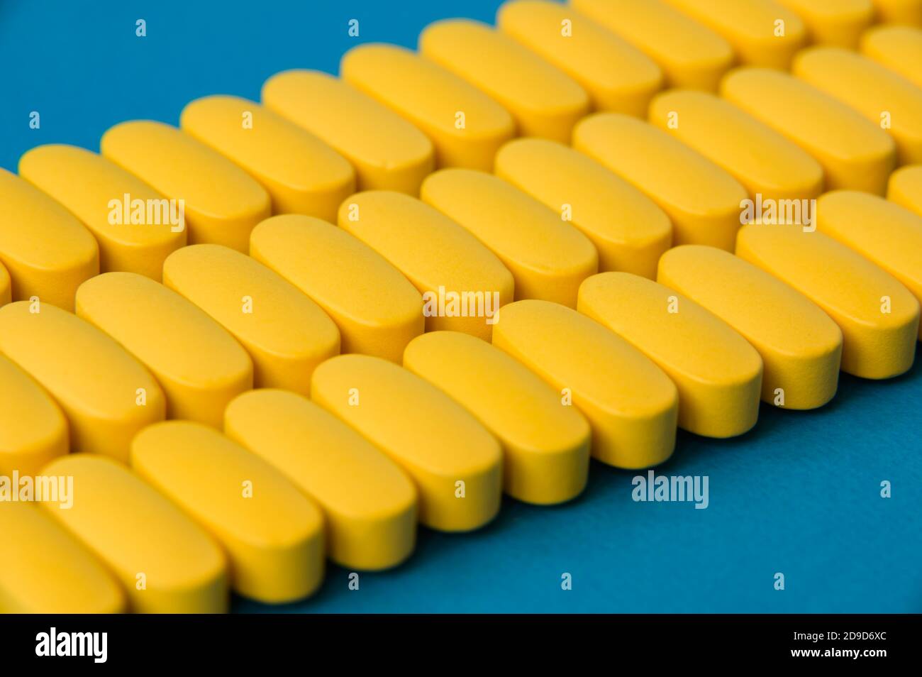 Pharmazie Produktionskonzept von drei Linien von vielen gelben Tabletten Pillen Medikamente auf blauer Oberfläche Stockfoto