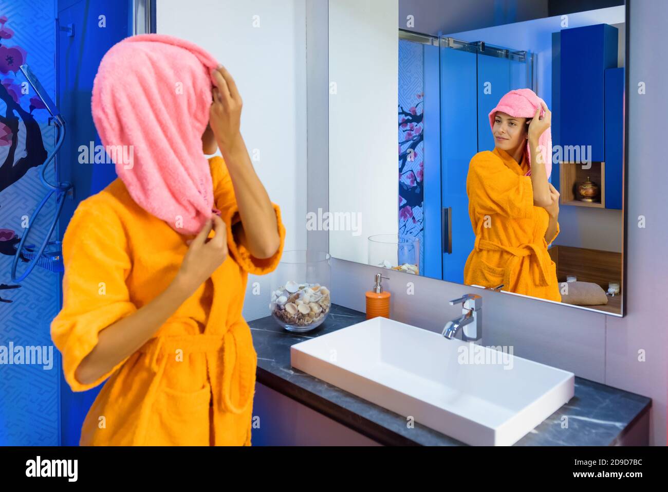 Junge Frau in hellen Bademantel Blick auf sich selbst in der Spiegel im Badezimmer, während sie sich um ihre Waschungen und Toilettenartikel Stockfoto