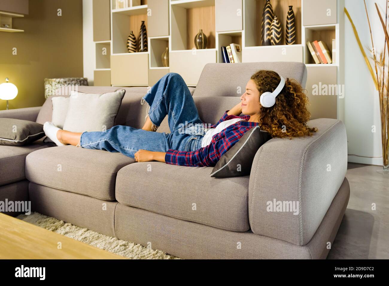 Junge Frau entspannt Musik zu Hause hören auf liegend Ein bequemes Sofa im Wohnzimmer mit einem Lächeln Des Vergnügens Stockfoto