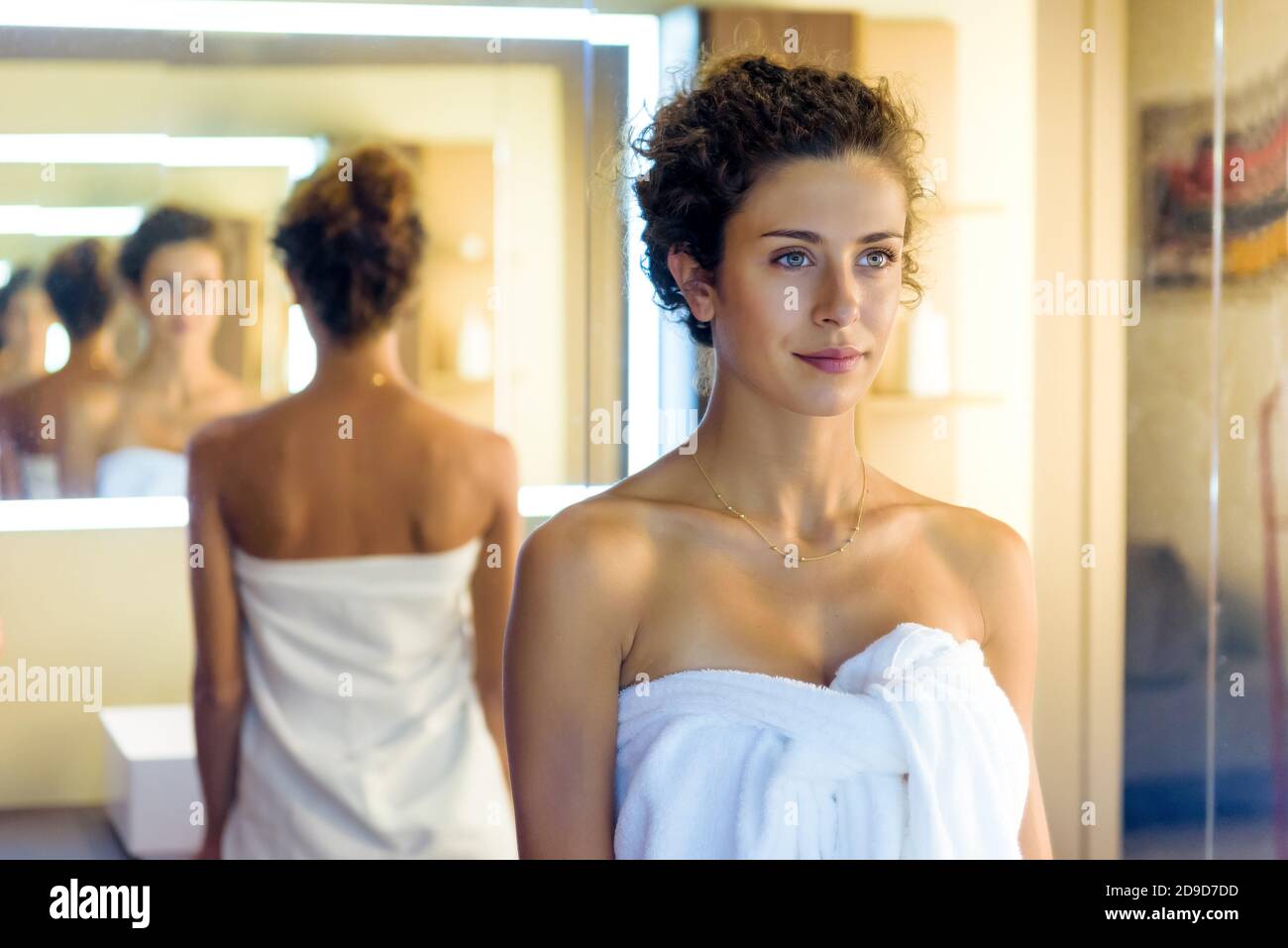 Junge Frau in ein sauberes weißes Handtuch eingewickelt, das sich selbst reflektiert Mehrere Male in parallelen Spiegelungen in einer abnehmenden Perspektive in Ein Badezimmer Stockfoto