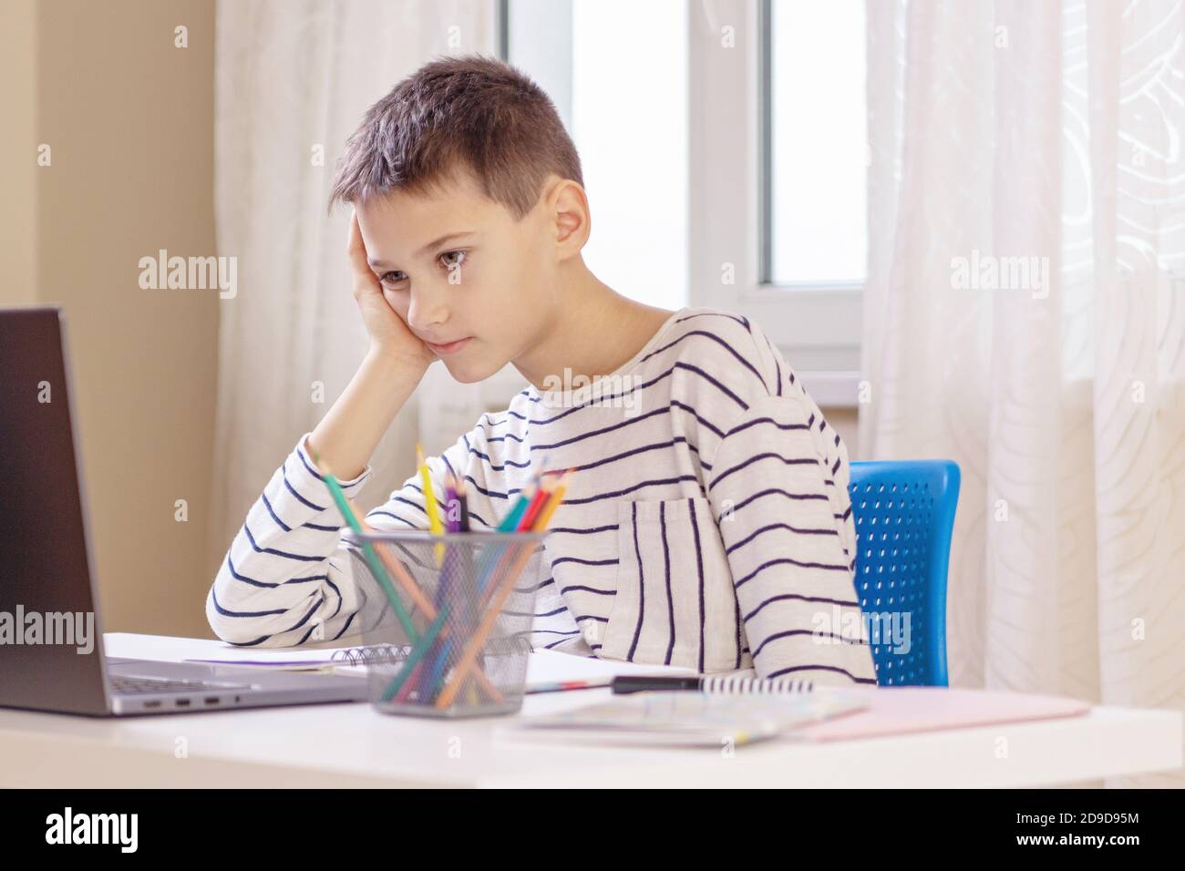 Trauriger, müder Junge, der zu Hause mit Büchern und einem Laptop am Tisch sitzt. Lernschwierigkeiten, Online-Bildungskonzept Stockfoto