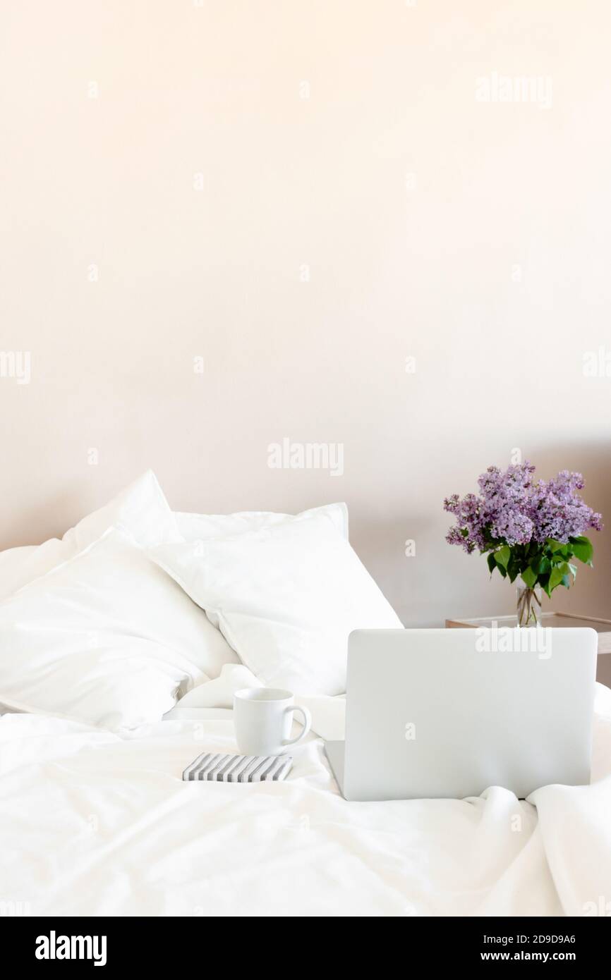 Helles Zimmer mit Laptop, Becher und Notizblock im Bett. Stockfoto