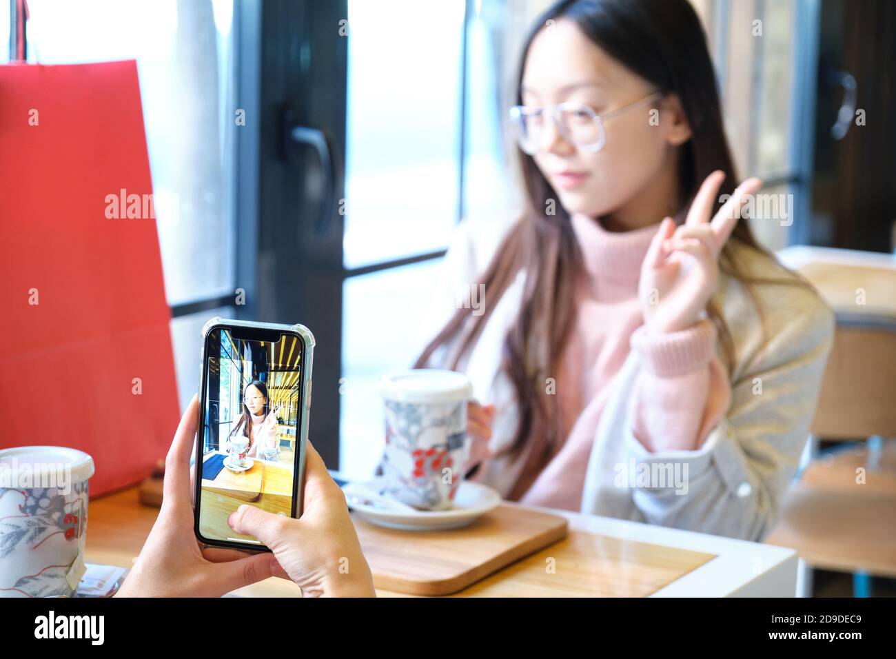 Junge kaukasische Frau, die ein Foto mit ihrem Smartphone von ihrem asiatischen Freund. Freunde in einem Café. Stockfoto