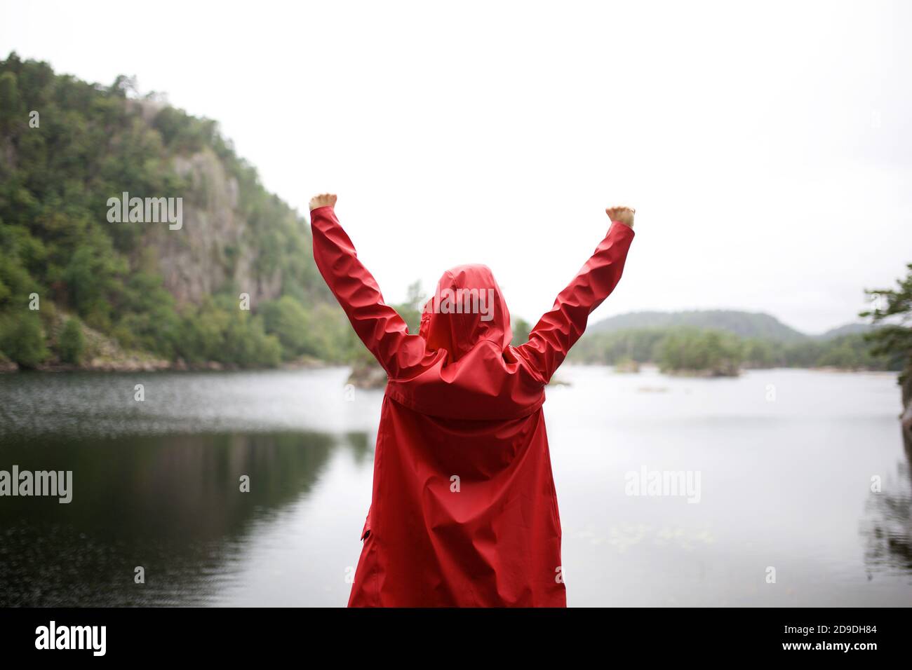 Porträt von hinten der Person mit roten Regenjacke Erhöhung Hände am See Stockfoto