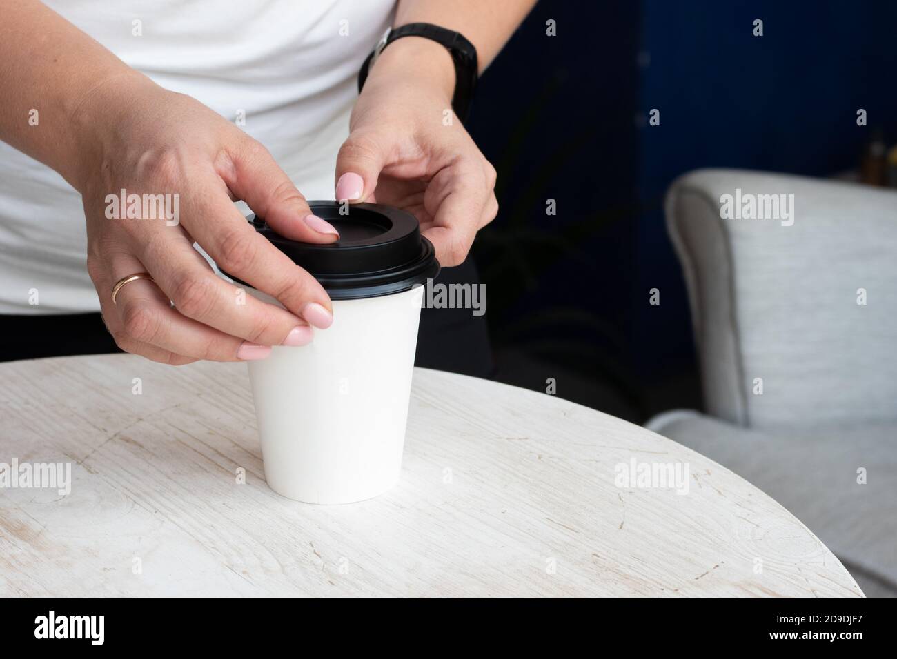 Weibliche Hände legen einen schwarzen Deckel auf eine weiße Papiertasse mit heißem Kaffee oder Tee, um draußen, Nahaufnahme genommen werden Stockfoto