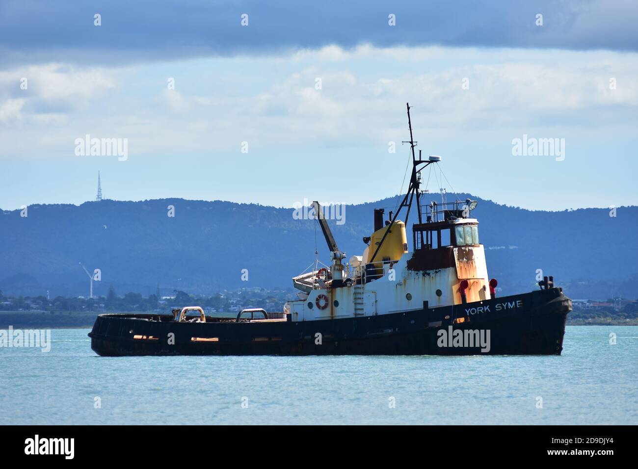 Schlepper mit schwarzem Rumpf und weißer Kabine mit Rostspuren auf der Oberfläche des ruhigen Hafens. Stockfoto