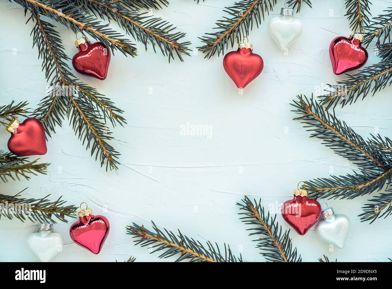 Rahmen aus Zweigen eines Weihnachtsbaums und Glasdekorationen in Form von Herzen. Stockfoto