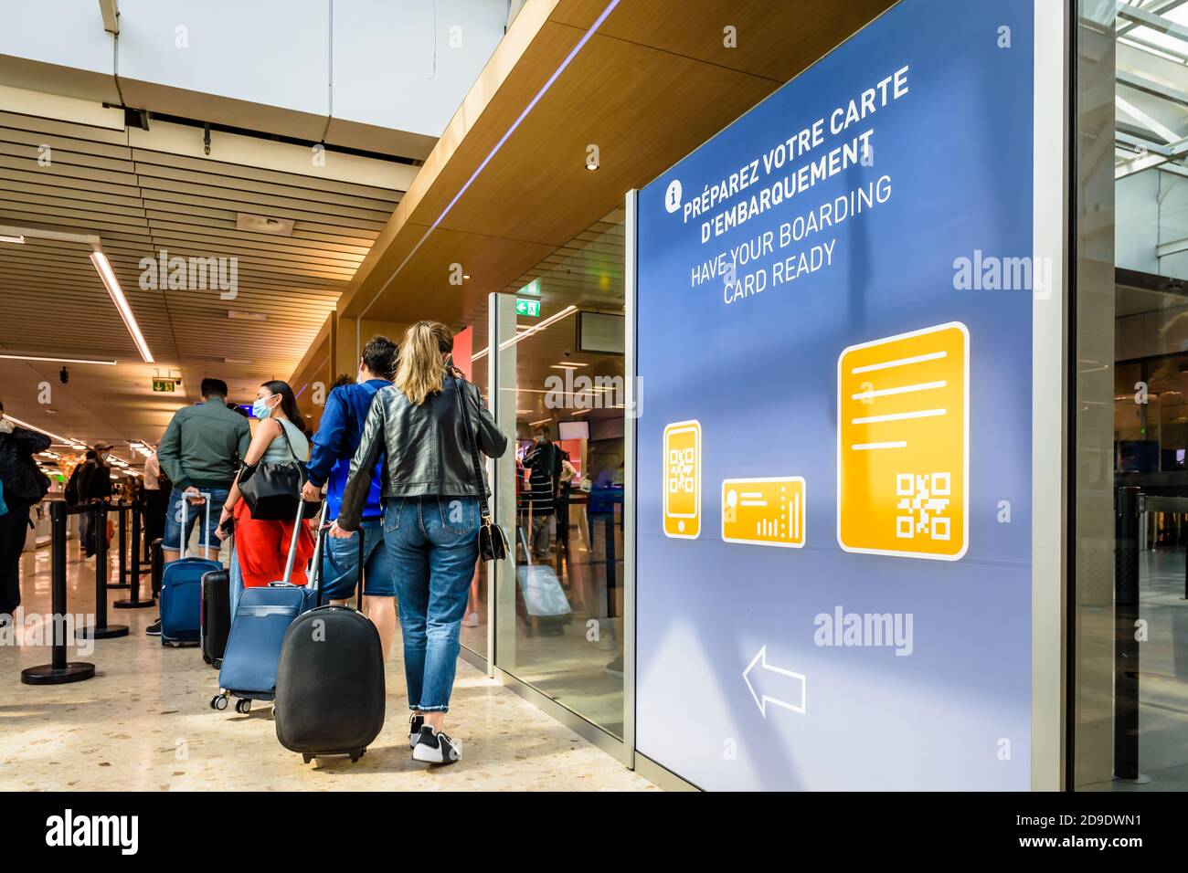 Passagiere mit Kabinenschleppen, die an einem Kontrollpunkt Schlange stehen In der Flughafengebäude neben einem Schild, das sie einlädt Um ihre Bordkarte fertig zu machen Stockfoto