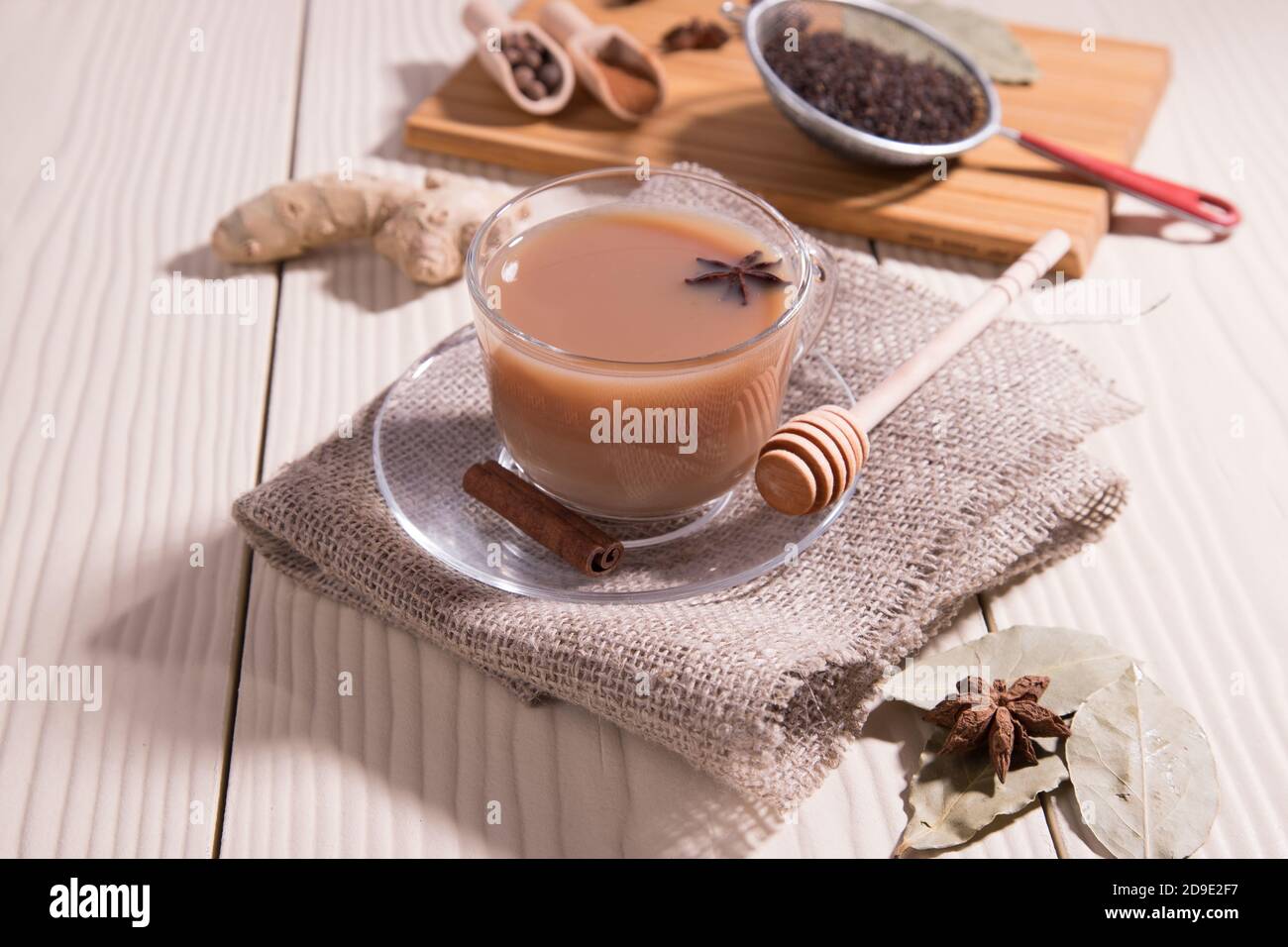 Eine Tasse heißen indischen Tee Masala Tee, Löffel mit Gewürzen auf einem Schneidbrett, auf einem weißen Hintergrund. Horizontale Ausrichtung. Stockfoto